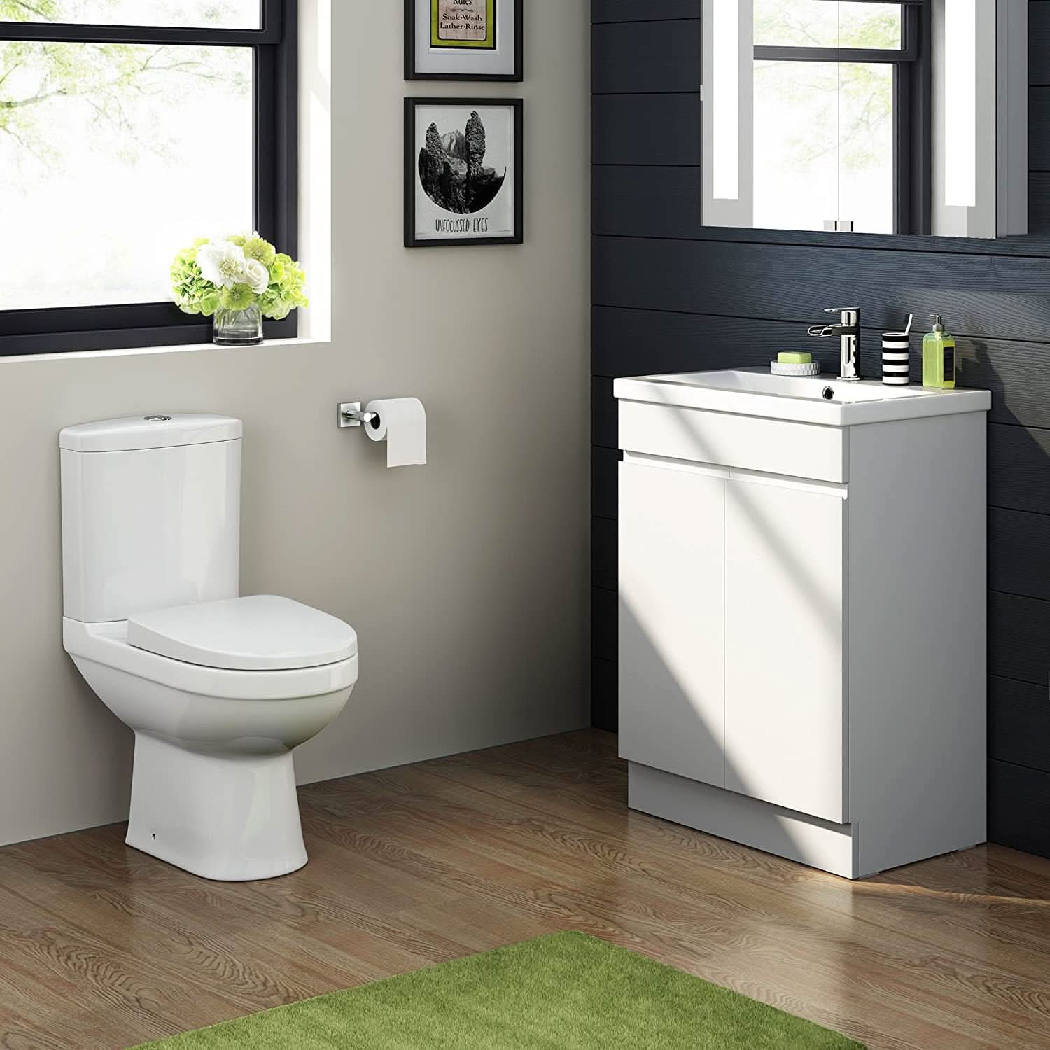 Modern bathroom featuring the iBathUK Trent Close Coupled Toilet & Vanity Unit with Basin, a gloss white WC pan, wall-mounted toilet paper holder, black-paneled wall, window with flowers, framed art, and a green rug on wooden floor.