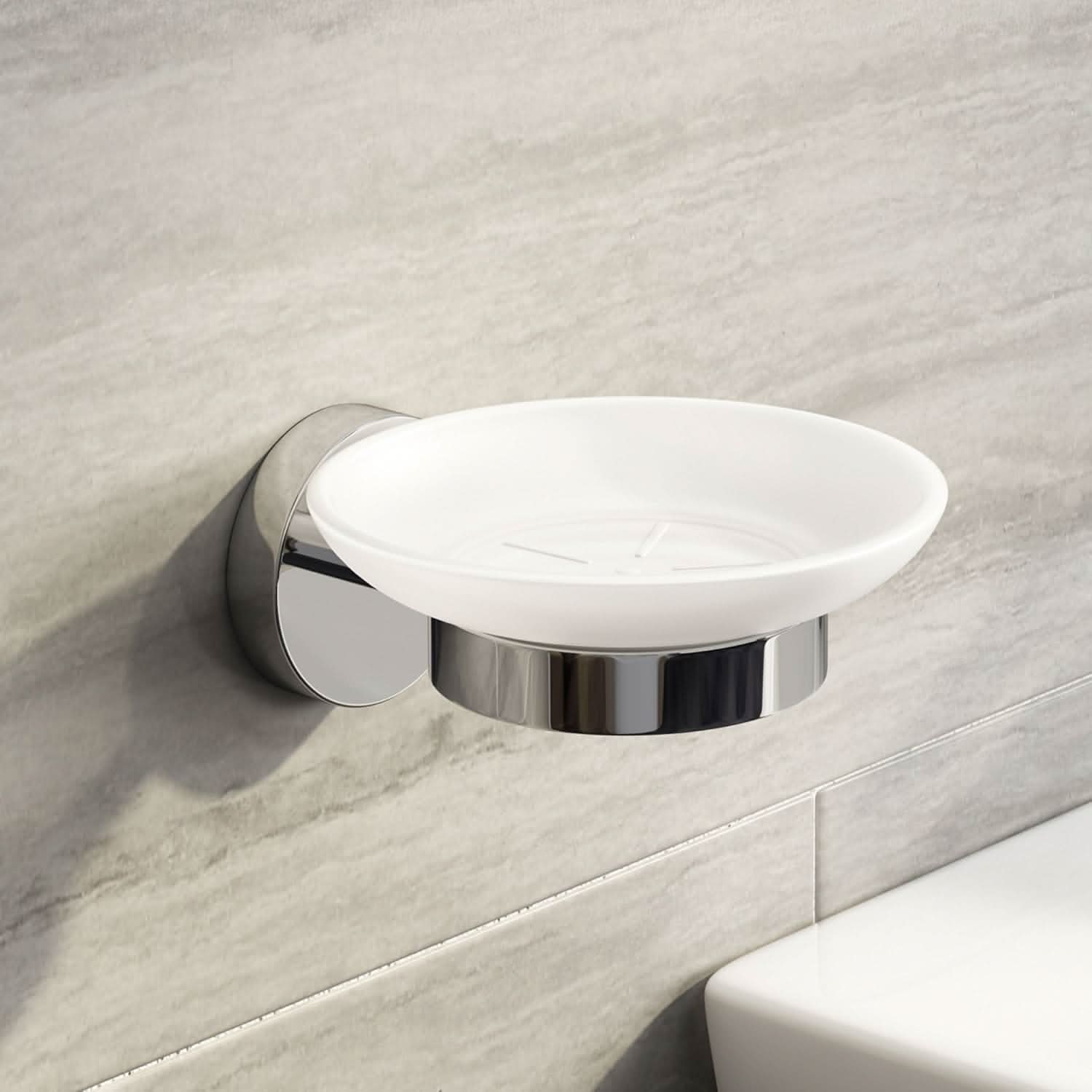 The iBathUK Lumo Designer Wall Mounted Soap Dish, part of a chrome accessory set with toothbrush holder and tumbler, features a white round tray and chrome base fixed above a white sink on a light gray tiled bathroom wall.