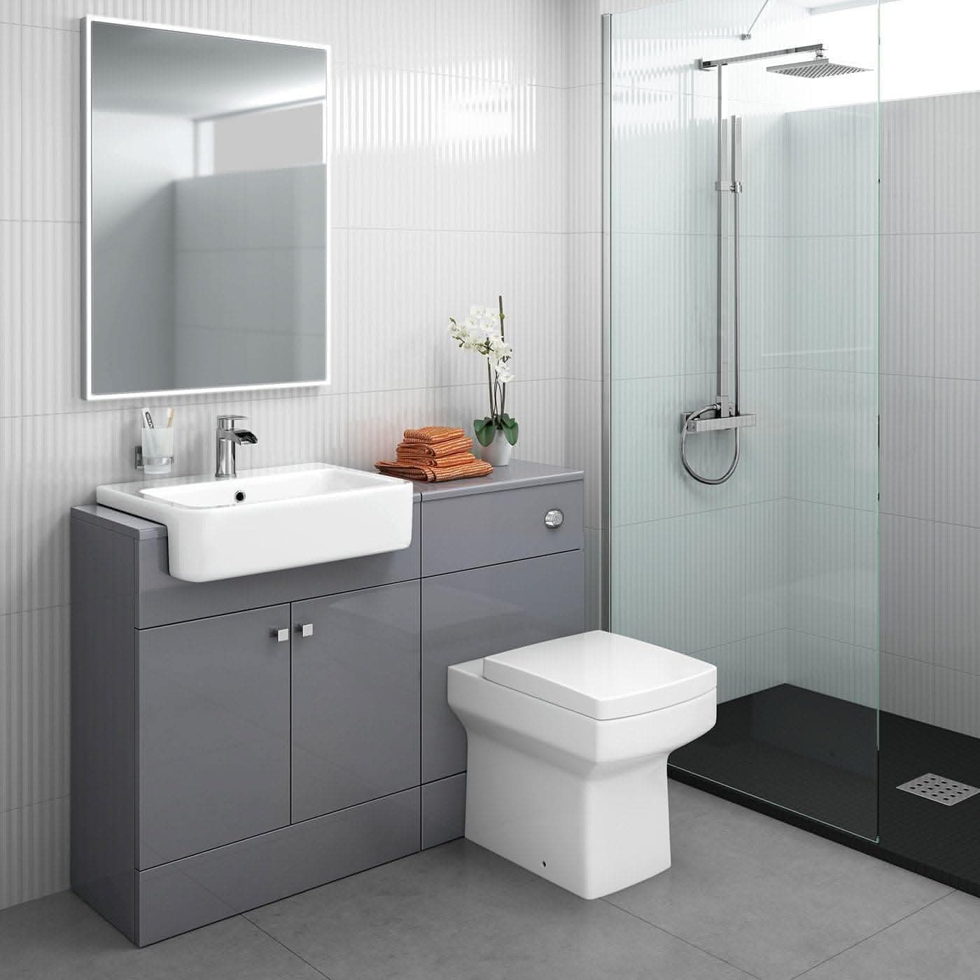Contemporary bathroom featuring the iBathUK Harper 2 Door Floorstanding Vanity Unit with 660mm x 800mm semi recessed basin, square toilet, glass shower, a mirror, faucet, orange towels, and an orchid atop a light gray floor and walls.
