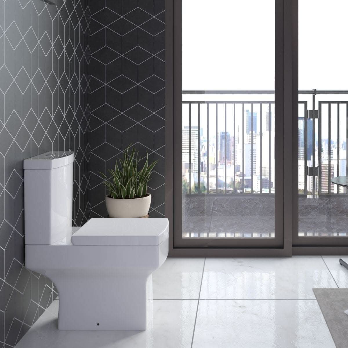 This modern bathroom showcases geometric dark gray wall tiles, a potted plant on the toilet, and city views. The iBathUK Avon Modern Bathroom Suite - Gloss White pairs seamlessly with the shiny light floor for a sleek look.
