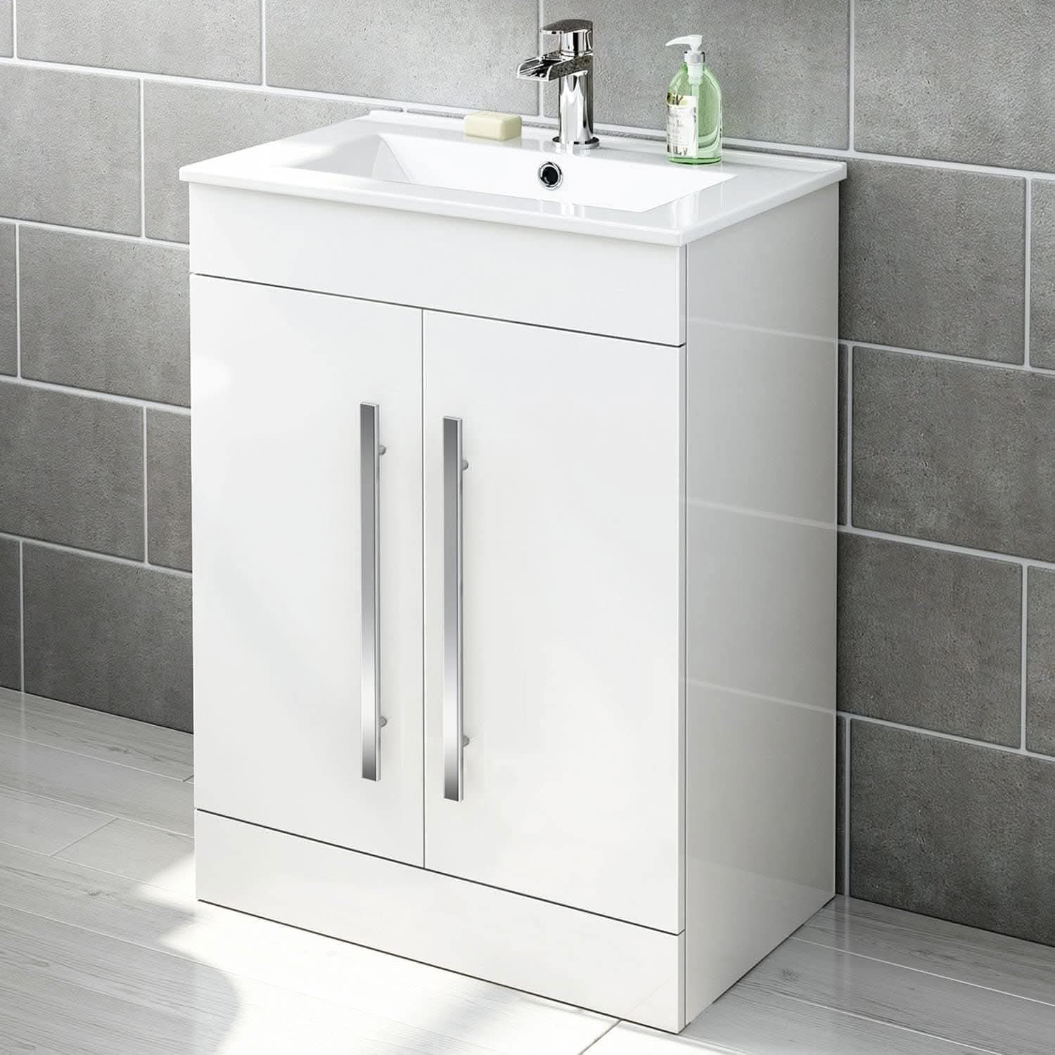 The iBathUK Avon Modern Bathroom Suite - Gloss White features a modern vanity unit with two doors and sleek silver handles, topped with a white basin and soap accessories, set against gray tiled walls.