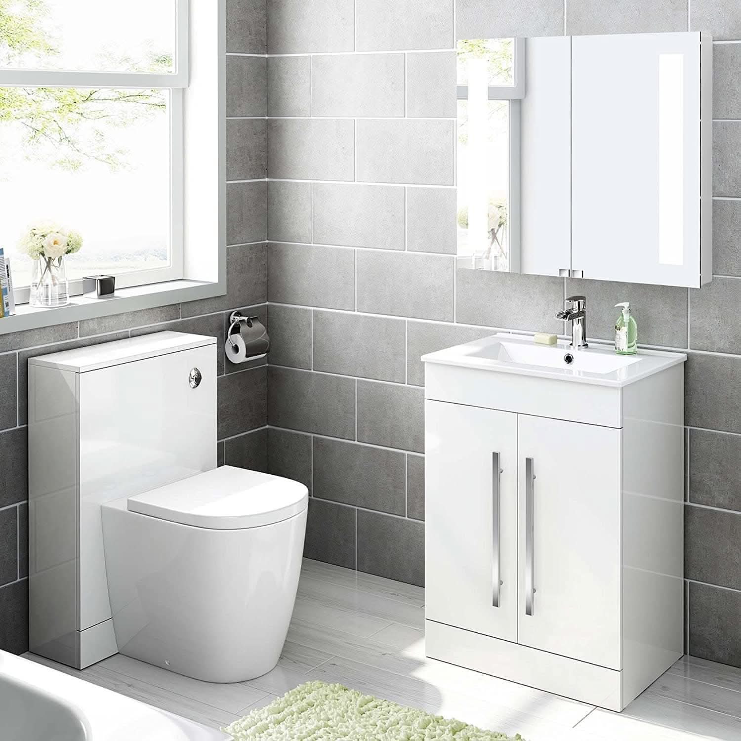 Modern bathroom with gray tiles, a white toilet, mirrored cabinet, and window with greenery. Features the iBathUK Avon 2 Door Floorstanding Vanity Unit With Basin (615mm x 815mm) and a light green bath mat on the white floor.