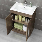 The iBathUK Avon 2 Door Floorstanding Vanity Unit With Basin (615mm x 815mm, 1 Tap Hole) features a modern wood cabinet with silver handles. Its open doors show neatly stacked towels and organized skincare items on the shelves.
