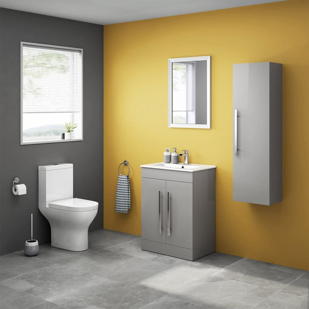 Modern bathroom with a yellow accent wall, grey floor tiles, white toilet, and the iBathUK Avon 2 Door Floorstanding Vanity Unit With Basin (615mm x 815mm, 1 tap hole). Features a tall wall cabinet, round mirror, and window with blinds for natural light.
