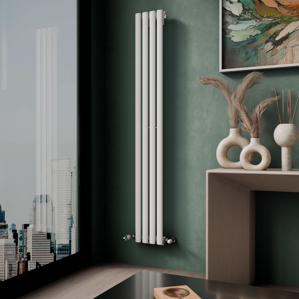 A modern corner features the iBathUK Princia Vertical Single Oval Panel Radiator on a green wall by a window with city views. A light wood table with decorative vases and framed abstract art enhance the stylish setting.
