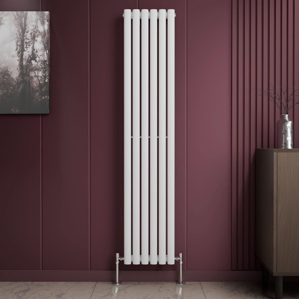 The iBathUK Princia Vertical Single Oval Panel Radiator in white stands against a burgundy panelled wall beside a brown cabinet and wall art. The light-toned floor features a subtle marble pattern.