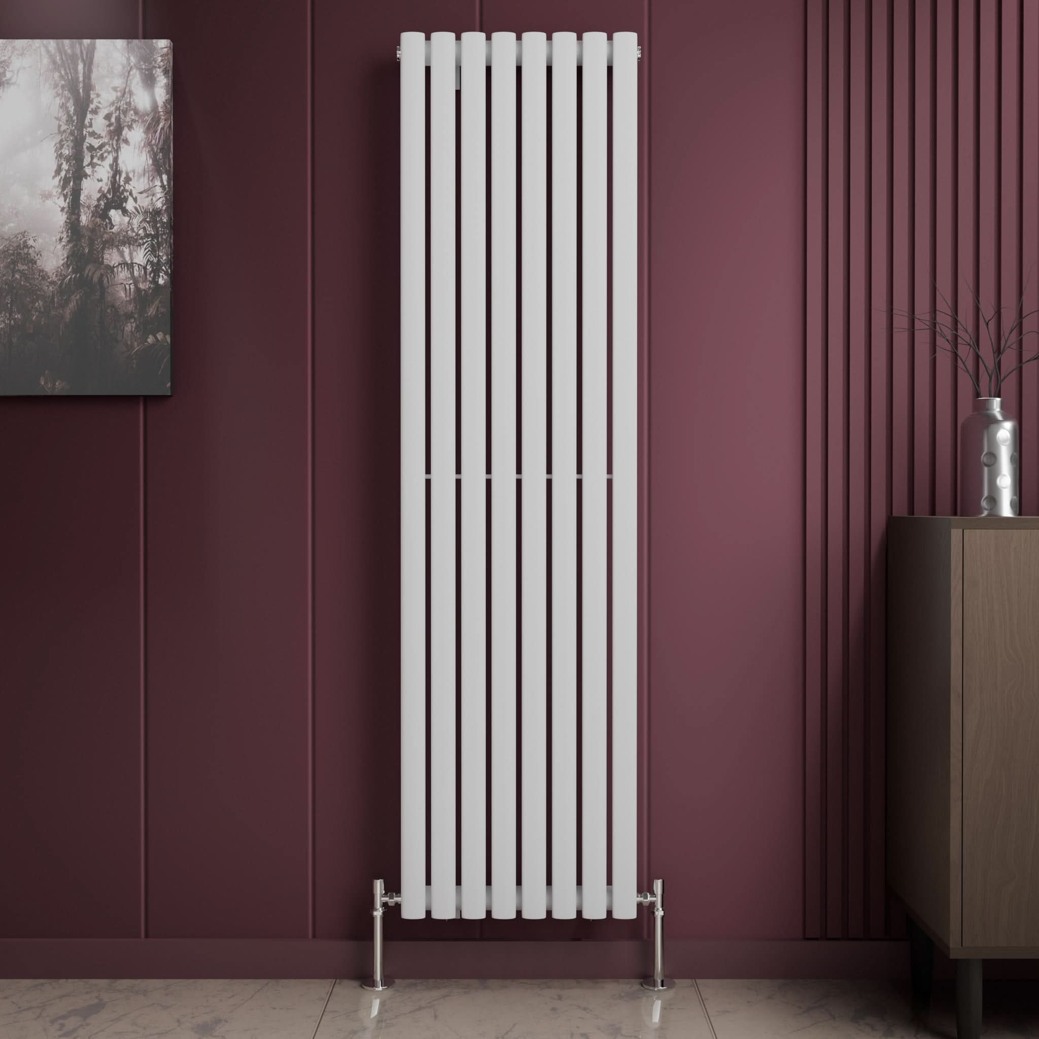 A Princia Vertical Single Oval Panel Radiator by iBathUK, in white, is mounted on a maroon wall. The room has a small cabinet with a silver vase, framed picture, and a light-colored floor.